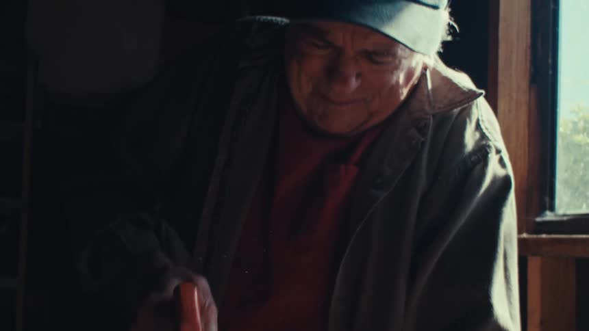 An image of an elderly man cutting a wood with a saw