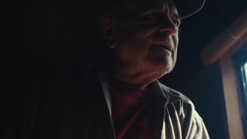Elderly man sawing while in his workshop stops to stare out the window