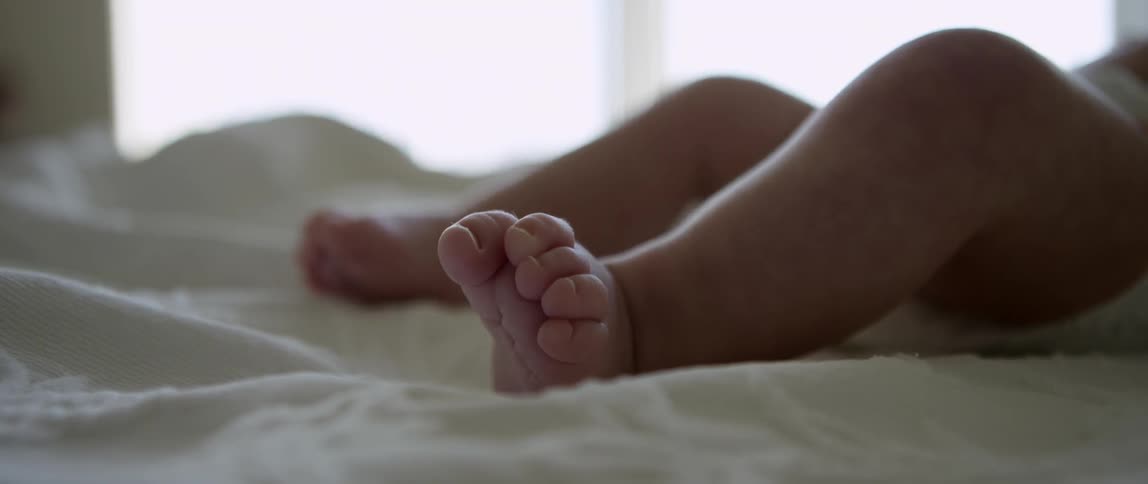 A baby moves his legs around on a white blanket