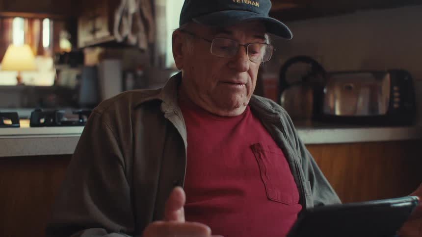 Elderly man sitting at kitchen table interacting with a tablet