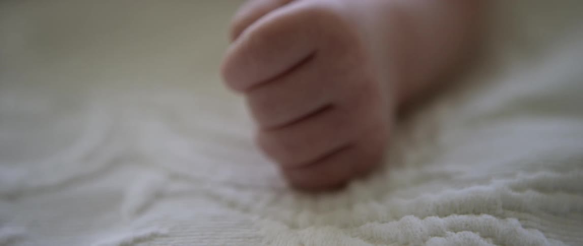 A baby's closed fist rests on a white blanket