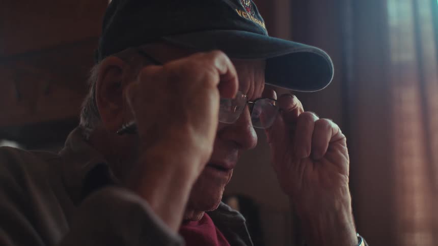 Elderly man sitting in a cap and putting on glasses