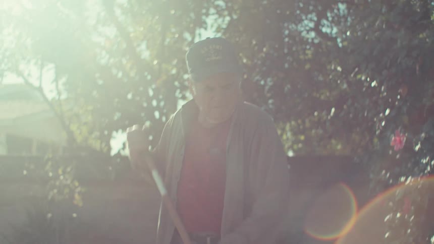 Elderly man in cap cleaning in backyard of house