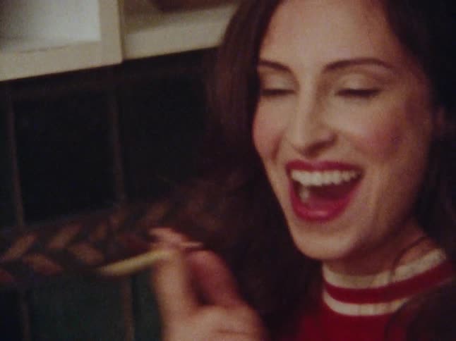 A beautiful woman laughs loudly and then smokes a cigarette in a kitchen