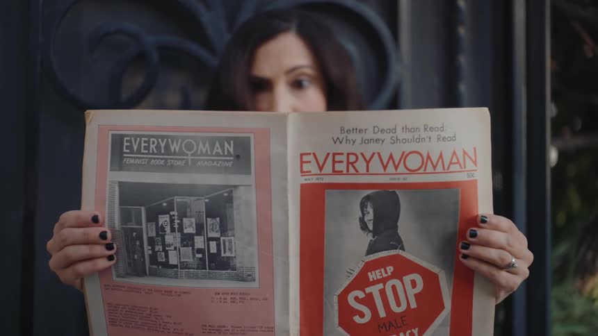 Woman in a red blouse picking up a newspaper and reading