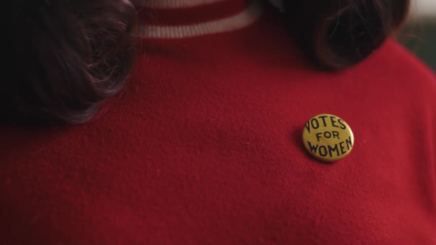 A woman attaches a button to her sweater