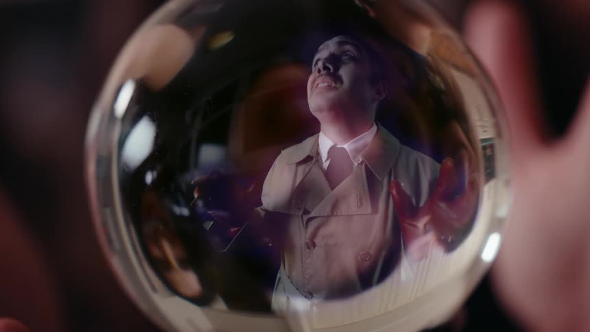 Face of a laughing woman watching a desperate gloved man in a glass globe