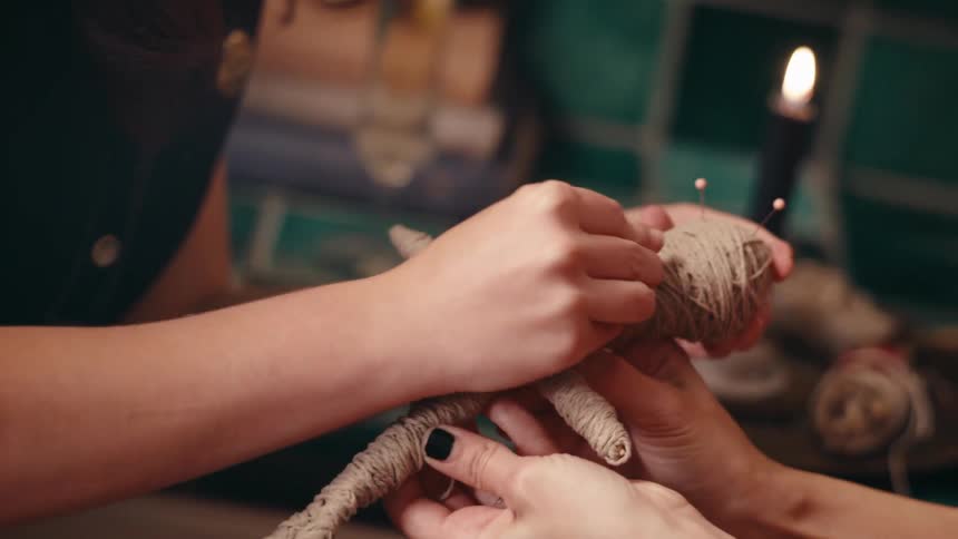A female holds a voodoo doll as another girl stabs pins into it