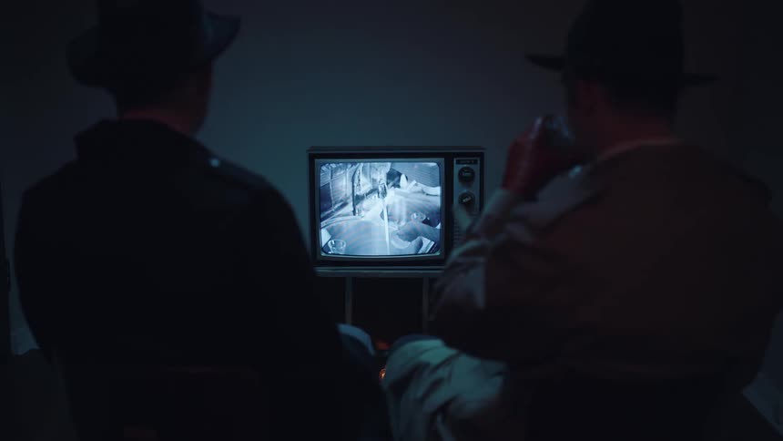 Two men drink while watching a television in a dark room