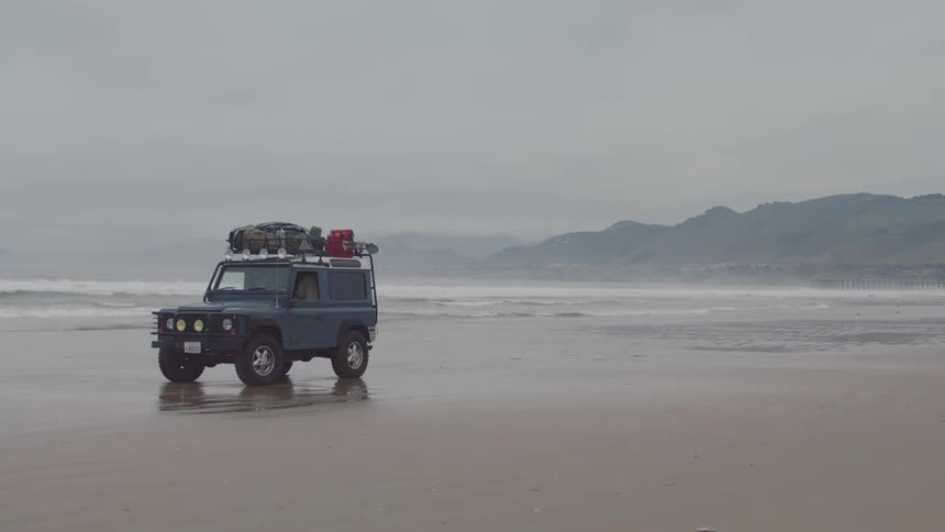 A blue jeep is parked on the beach on a foggy day