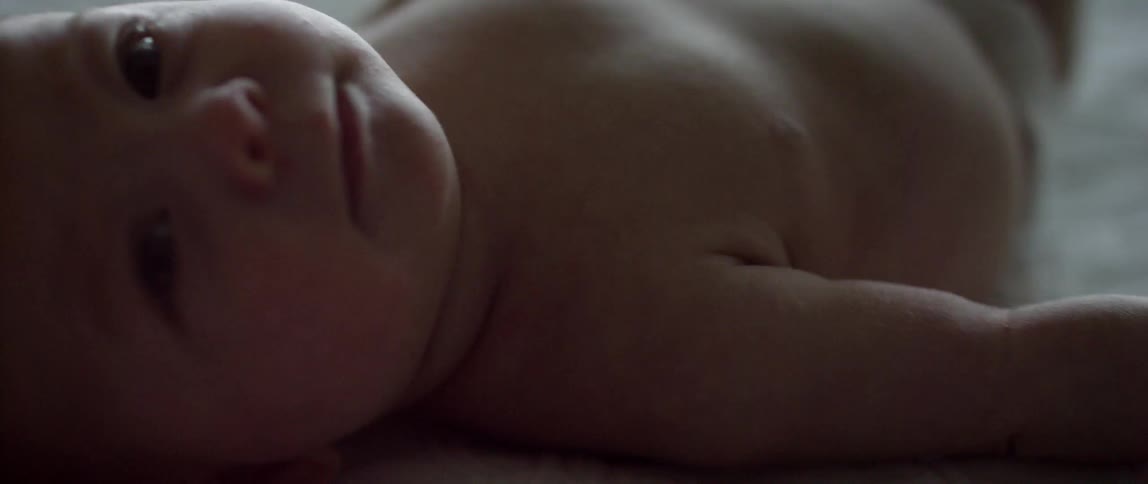 A baby moves his arm and head around while laying on a white blanket