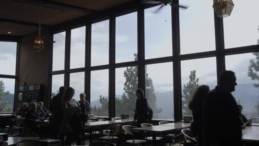 Several people are standing around tables in a room with large windows