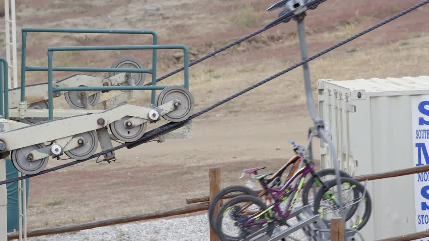 A machine with many wheel turning a belt and lifting a couple of bikes up that are on a shelf
