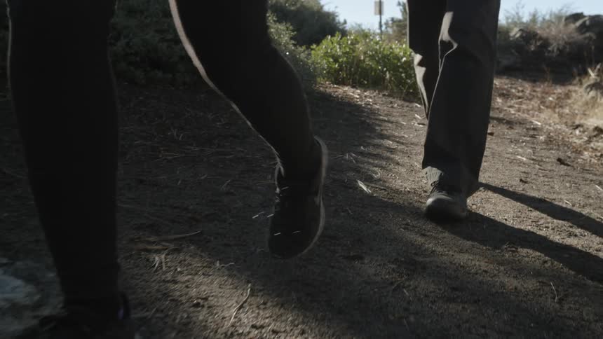 Two people are walking along a dirt trail