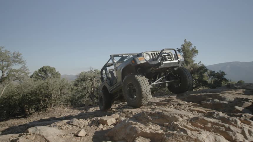 A jeep is driving over a rocky path up a hillside