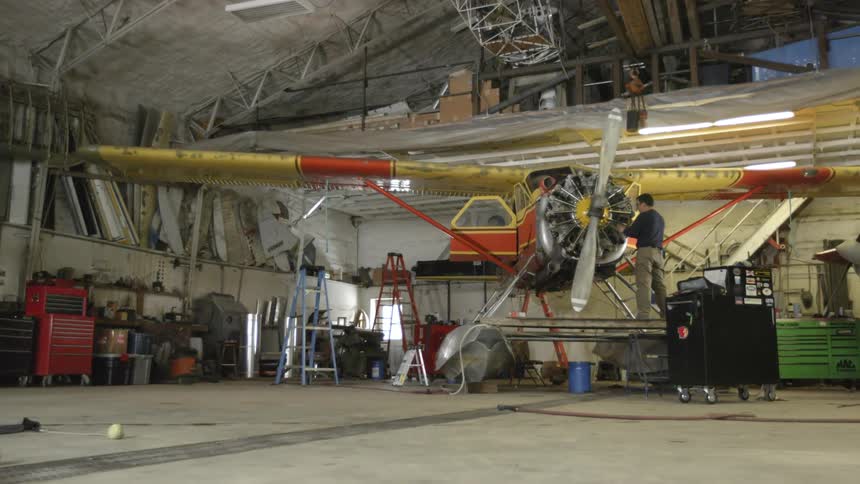A man is working on a single engine plane in a hangar