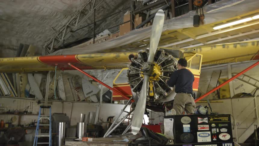 A man adjusts the propeller on a small yellow plane