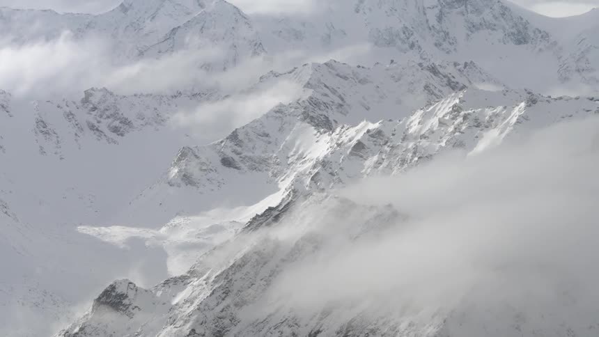 Pending view of snow-covered mountains with clouds hovering towards the top of them