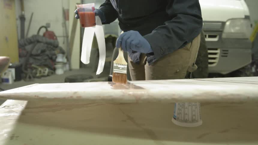 A man is painting a liquid onto a molded piece in a garage