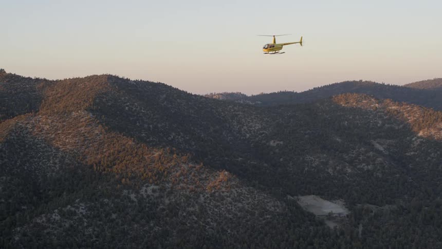 A helicopter is flying over mountains near dusk