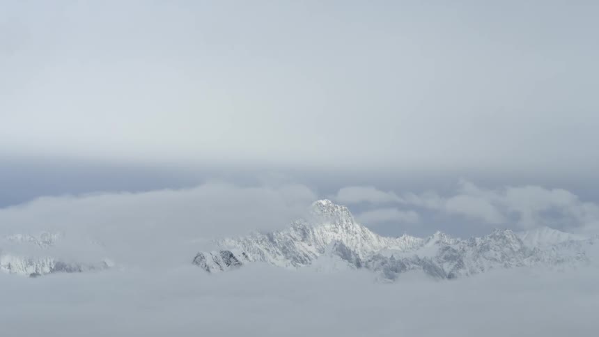 Clouds hover over and beneath a tall mountain peak