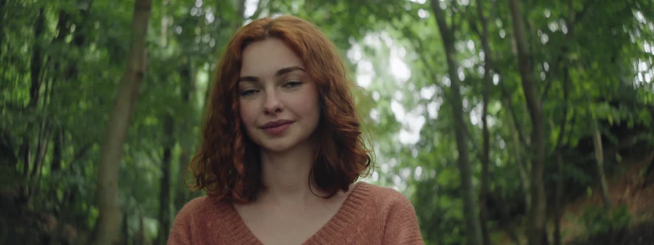 Portrait of a young redhaired woman in an environment surrounded by trees during the day