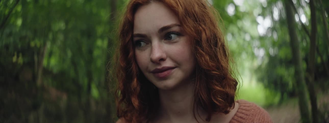 A young woman with red hair looking to her right side and she is in an environment that is full of trees around