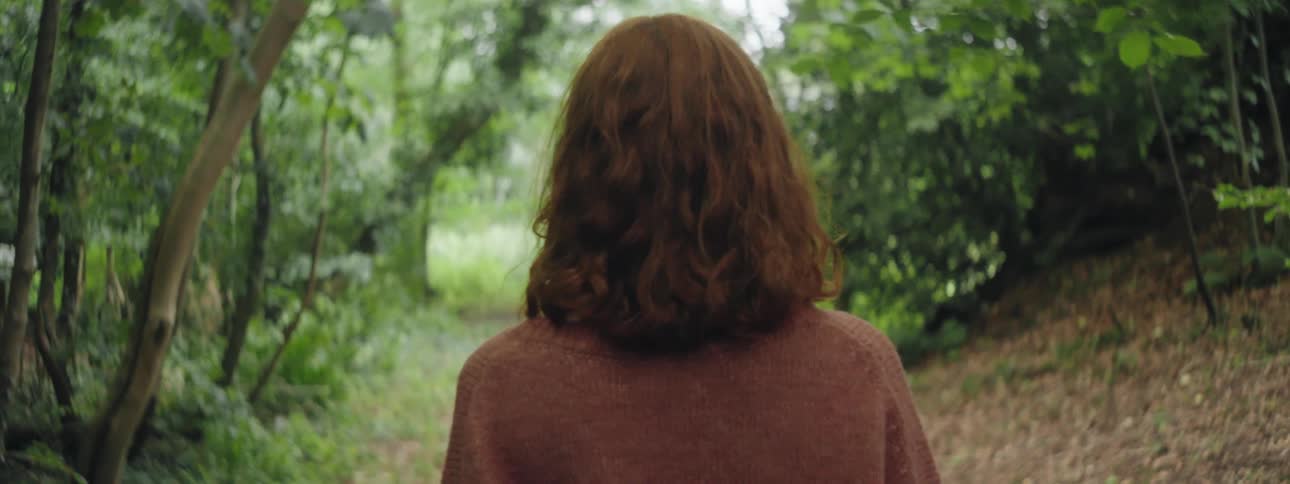 A back clip of a blond lady walking in the woods