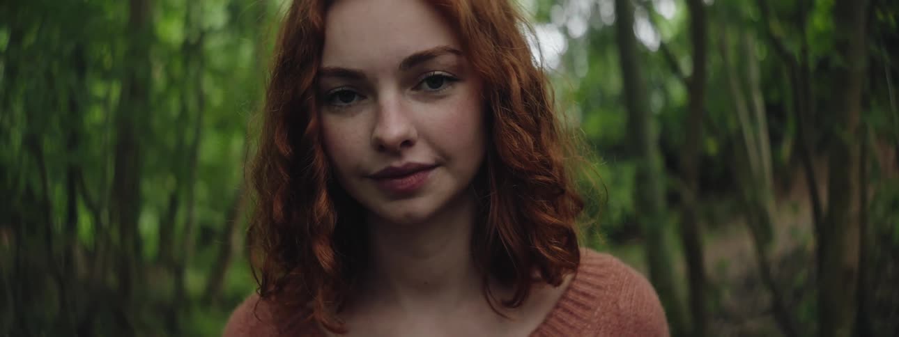 A woman with curly hair smiles while standing within a grove of trees