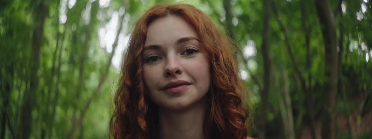 A happy woman with red curly hair looks around in the woods