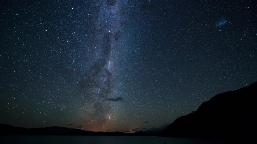 Starfilled night sky with the milky way visible as a dense cluster of stars and silhouettes of hills