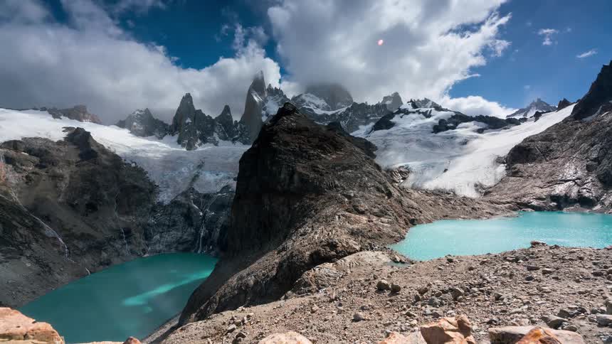 A range of snowcovered mountains and closer to the base there are mountains that do not have snow and there are two lakes with blue water