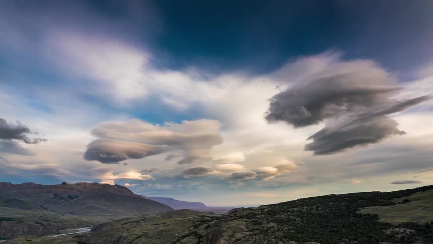 Dark storm clouds form and fall apart over a mountainous area with a river flowing through a valley
