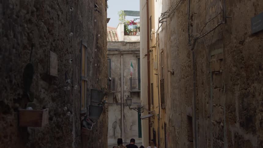 Four males walk in a narrow space between two oldlooking buildings