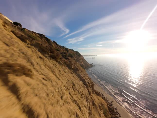 A stunning coastal landscape with a towering cliff overlooking a sandy beach and the vast ocean stretching towards a clear blue sky