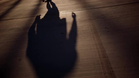 A long shadow of a person rides a skateboard in a suburban street at night