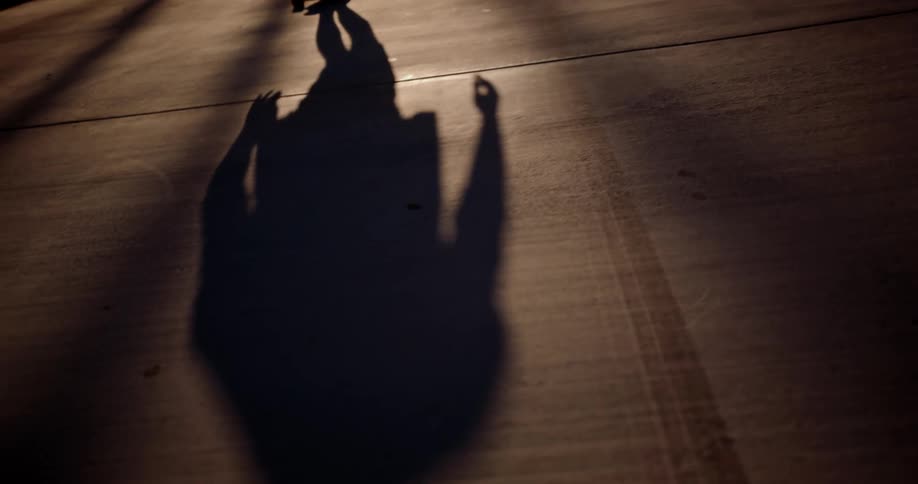 A long shadow of a person rides a skateboard in a suburban street at night