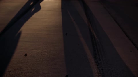 Two people casting shadows walk across a street at night
