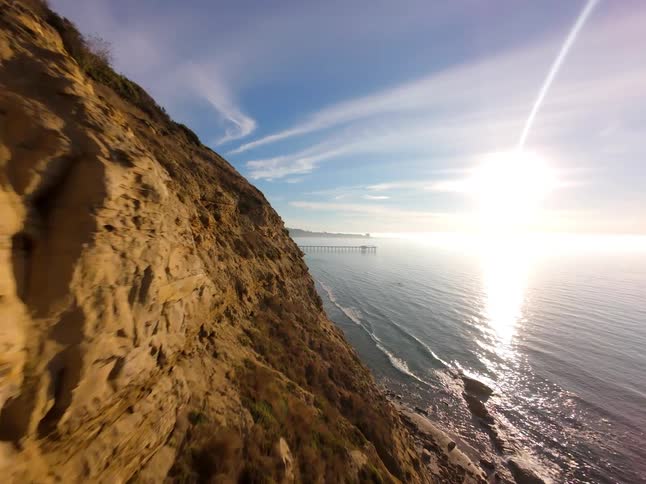 Aerial view of a rocky coastline on the edge of a beach with a pier in the background