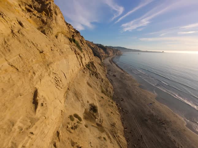A steep cliff looms over a beach and tidal waves flowing in