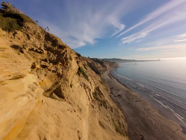 A stunning coastal landscape with a dramatic cliff overlooking a sandy beach and the vast ocean stretching towards a clear blue sky