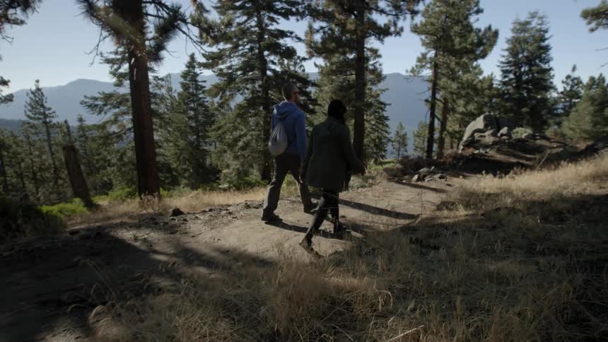 A man and woman are walking down a dirt trail during the day