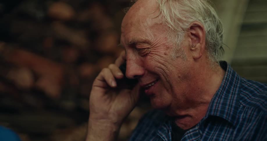 Elderly man wearing a blue shirt talks on the phone laughing