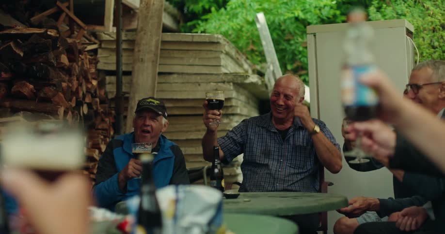 Group of men sitting around a table and holding glasses of beer and celebrating happily