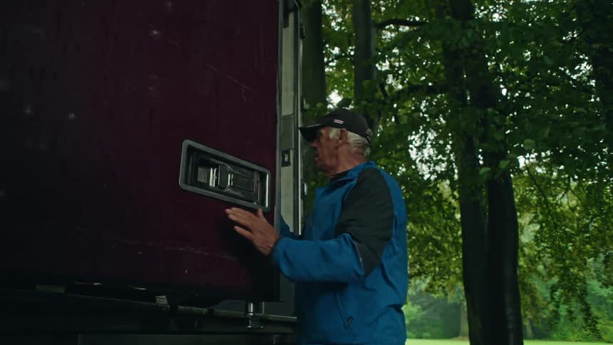 A delivery man opens the back door to his truck while two other people walk past