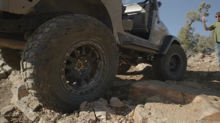 A person guides a jeep over some large rocks