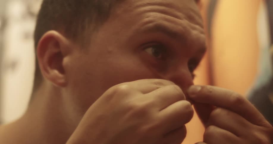A man pops several pimples on his nose in a bathroom