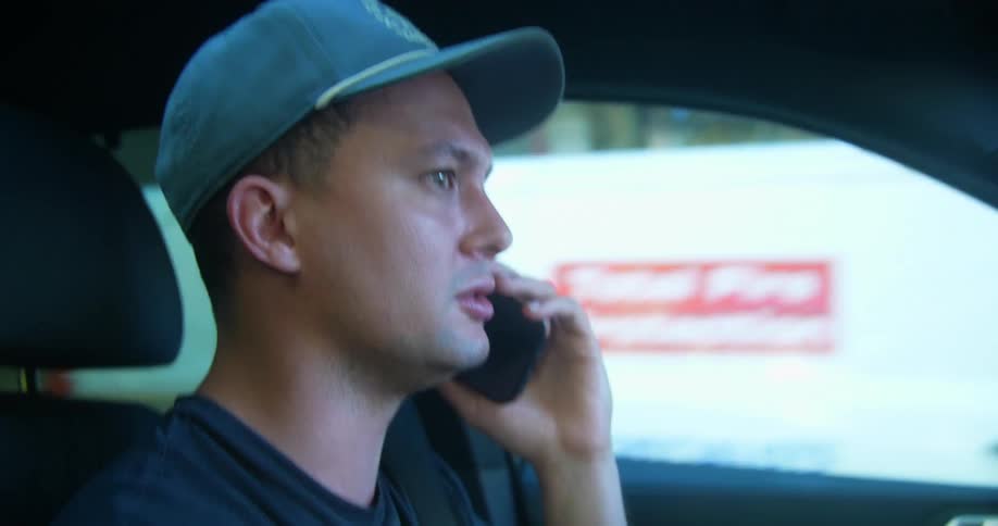A man drives down a city street while speaking on a smartphone