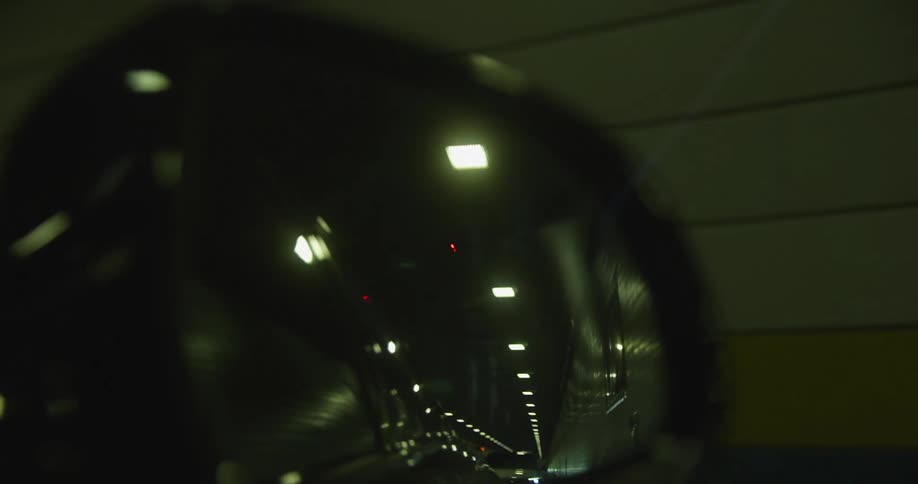A rear view mirror of a vehicle reflecting a tunnel with lights on the roof