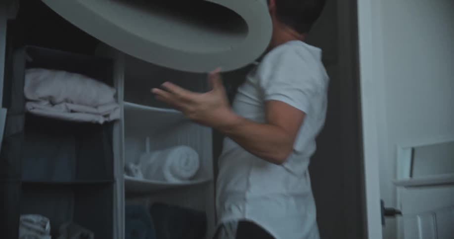 A man picks up a large piece of foam and jams it into a space in a closet